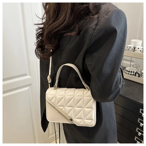 Detail view of cream quilted crossbody bag with gold metal trim on model