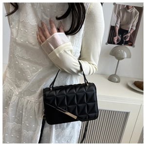 Detail of black quilted crossbody bag with gold metal hardware on minimalist background