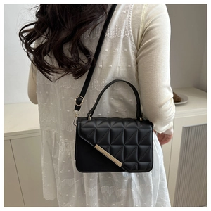 Detail of black quilted flap crossbody bag with gold hardware shown on a model