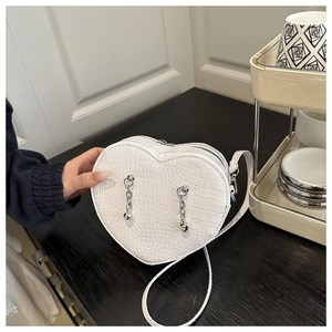 Detailed view of white heart-shaped handbag with crocodile texture and silver chains