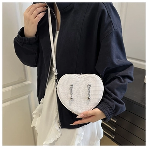 Detail of white heart-shaped crossbody bag with crocodile texture and silver metal chains