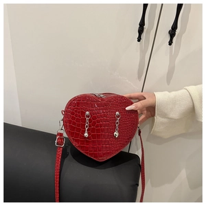 Detail of red heart-shaped shoulder bag with crocodile texture and silver chain charms