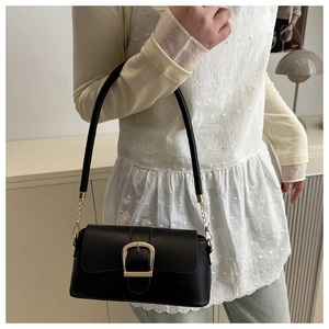 Detail of black leather shoulder bag with a large gold U-shaped buckle on a model