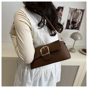 Close-up of brown vintage underarm bag with gold buckle and chain strap on shoulder