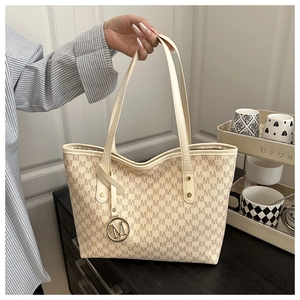 Detail of a beige tote bag featuring repeated M patterns and a circular metal charm