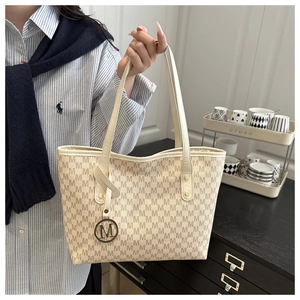Detail of a large cream tote bag with letter print and gold M charm held by a person