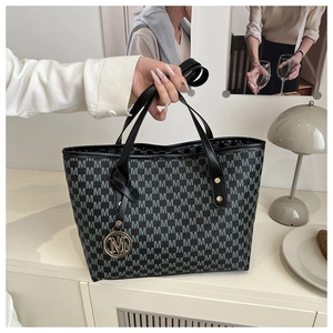 Detail of large tote bag with M-pattern print, leather handles and golden metal charm