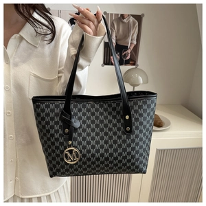 Detail of tote bag showing M-letter print and golden metallic charm on shoulder strap