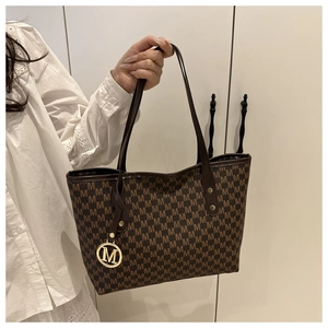 Detail of a large brown tote bag with M-pattern print and a gold metallic M pendant
