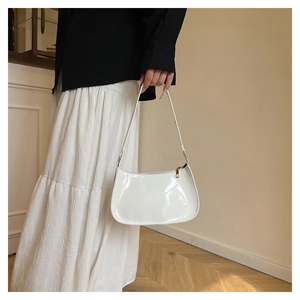 Close-up of white patent leather baguette bag worn with a black blazer and white skirt