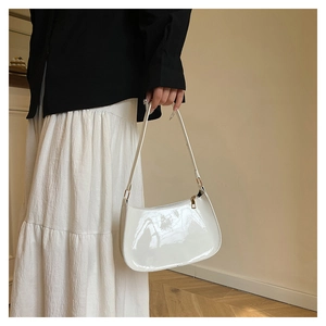 Gros plan du sac hobo en cuir verni blanc avec fermeture éclair dorée tenu par un modèle