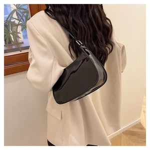 Close-up of a glossy black patent leather underarm bag with gold metal buckle detail