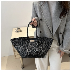 Close-up of leopard print tote bag with gold metal plaque held by a model in a grey coat