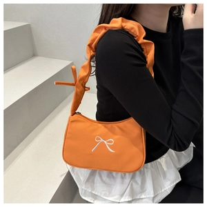 Detail of bright orange shoulder bag featuring white bow embroidery and ruffled strap