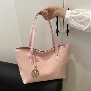 Pink tote bag with all-over M-pattern and gold-tone logo charm shown in hand