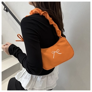 Detailed view of orange shoulder bag with bow embroidery and ruffled handle on model