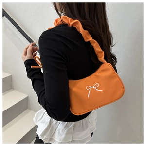 Detail of orange underarm bag with white bow embroidery and scrunchie shoulder strap