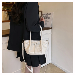 Close-up of cream PU leather handbag with decorative bow and adjustable shoulder strap
