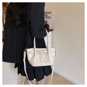 Detail of a creamy bow-knot shoulder bag with glossy finish and elegant pleats