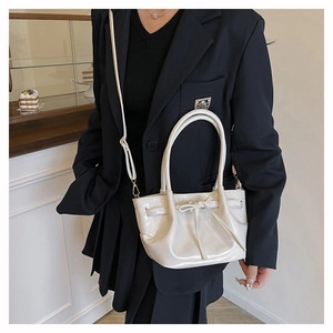 Detail of a beige pleated bucket bag featuring a decorative bow and adjustable strap