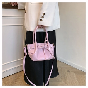 Detail of light pink patent leather bucket bag featuring a decorative bow and adjustable strap