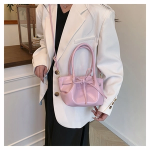 Detailed close-up of a pink glossy bow bag worn with a white blazer for styling
