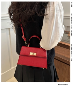 Detail view of red textured leather handbag with gold twist lock and adjustable shoulder strap