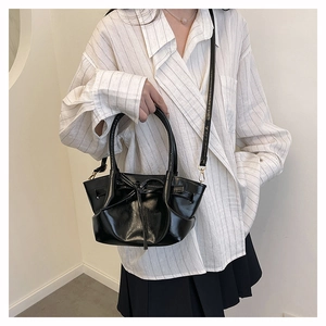 Detail of glossy black bow bucket bag showing the elegant drawstring knot and handle