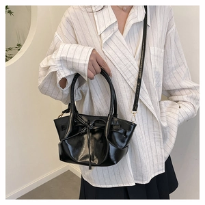 Glossy black bat-wing bucket bag with decorative bow shown as a crossbody detail
