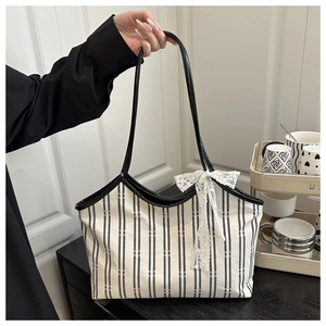 Close-up of striped canvas tote bag with black leather handles and white lace bow detail