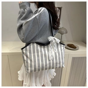 Detailed shot of striped canvas tote with white lace bow on minimalist gray clothing