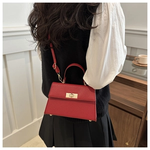 Red pebbled leather crossbody bag with gold lock shown on a model in a minimal interior