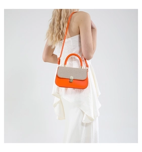 Detail of orange leather shoulder bag with beige woven flap and gold hardware