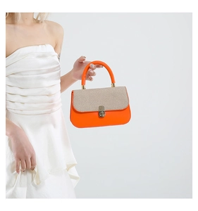 Detail of a chic orange underarm bag featuring woven texture and a round handle