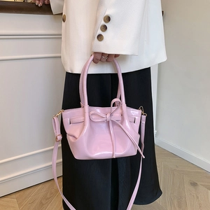 Pale pink glossy leather bow tote bag shown with a white suit and black skirt