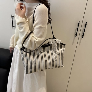 Striped canvas tote bag with lace bow detail and leather straps worn by model
