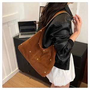 Detail of a large brown suede shoulder bag with gold metal rivets worn by a model