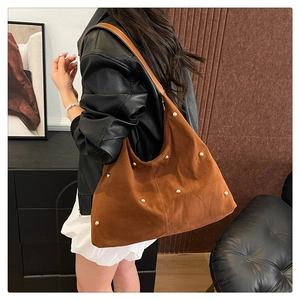 Close-up of brown suede shoulder bag with golden rivets worn over black leather jacket