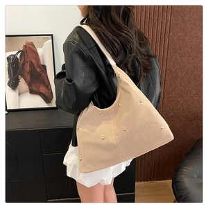 Detailed view of cream suede shoulder bag with gold rivets shown in a lifestyle setting
