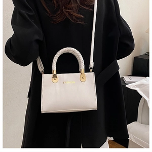 Beige rechteckige Handtasche mit geflochtenem Griff und Golddetails vor schwarzem Anzug