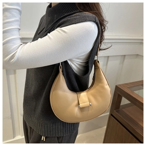 Detail of a light beige half-moon underarm bag with silver cylindrical metal buckle