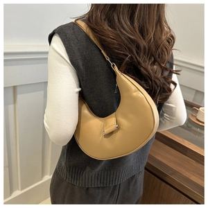 Minimalist beige crescent bag shown as a shoulder bag in a cozy cafe setting
