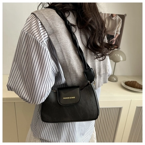 Detail of a black synthetic leather underarm bag with gold logo and twisted strap