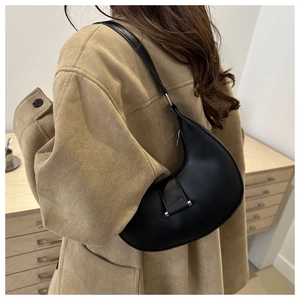 Rear view of a model wearing a black crescent-shaped underarm bag with a brown suede jacket