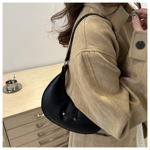 Side view of a black matte crescent hobo bag worn with a stylish khaki coat