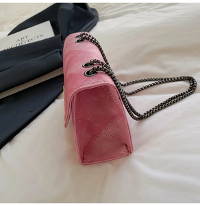 Detail of pink quilted crossbody bag showing metal chain strap and accordion side structure