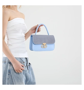 Detail of light blue shoulder bag featuring grey woven texture flap and gold circular buckle