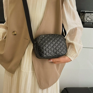 Sac bandoulière noir matelassé avec motif à losanges porté par un mannequin
