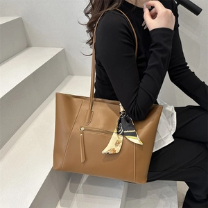Brown leather tote bag with decorative silk scarf on handle and front zipper detail