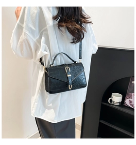 Detail of black crocodile pattern handbag with gold clasp and adjustable strap